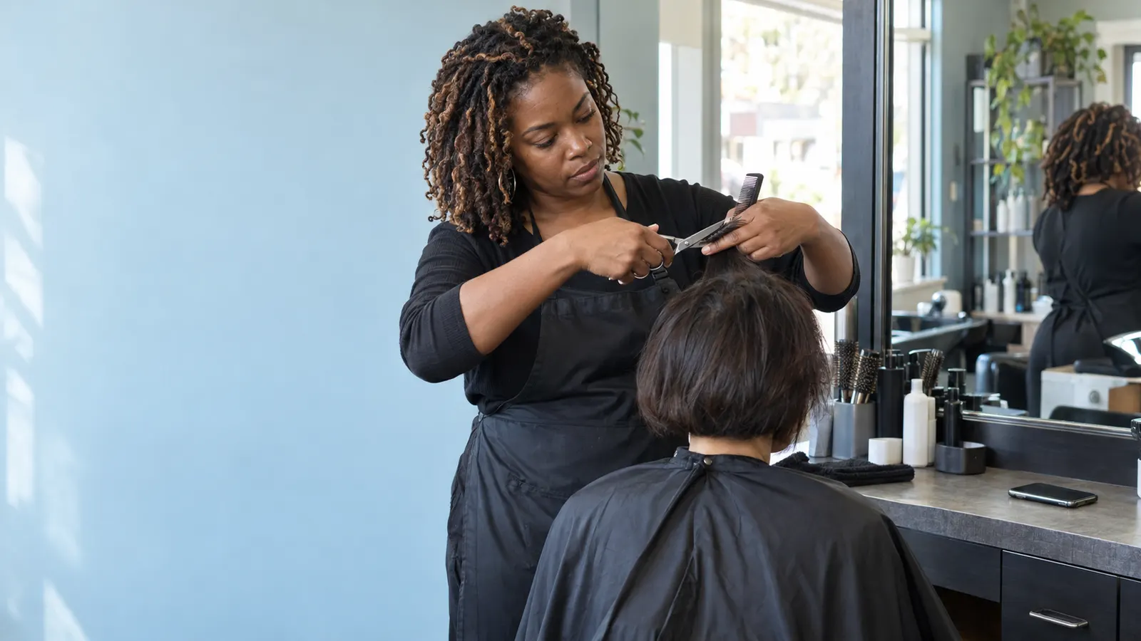 A stylist cutting a client’s hair with scissors and a comb in a bright salon